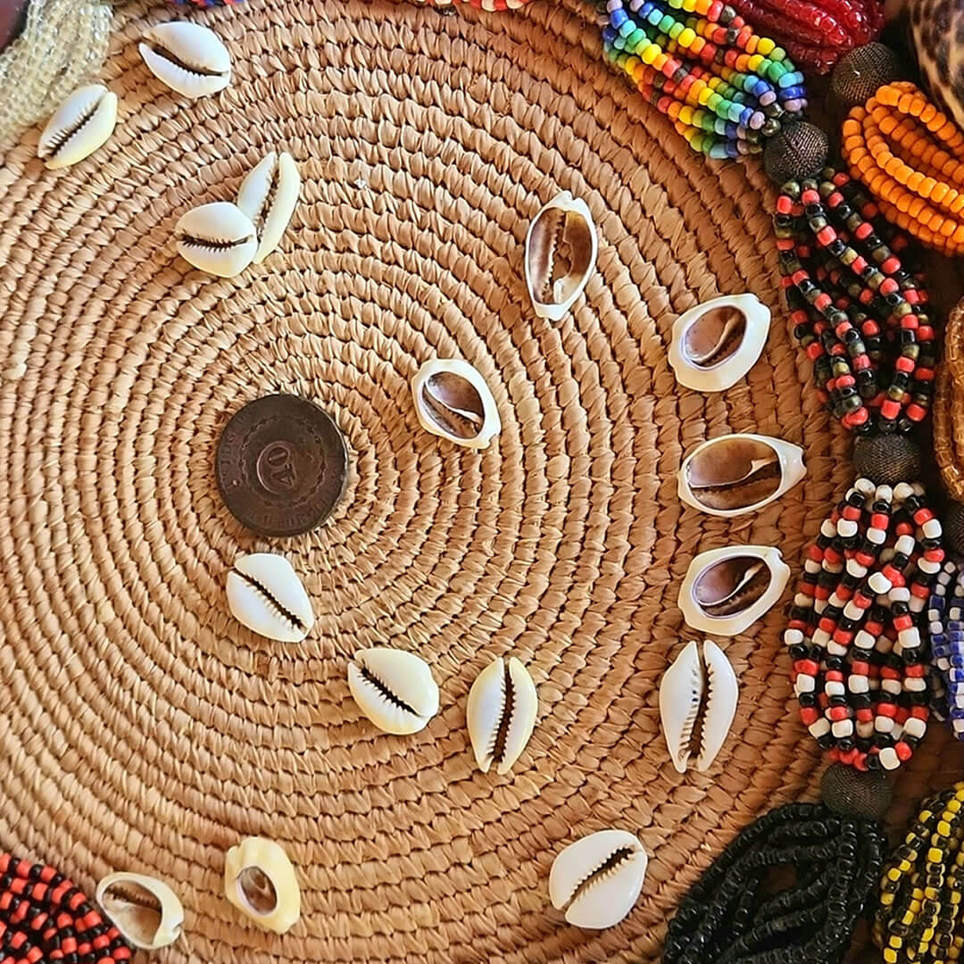 Jogo de búzios: búzios dispostos sobre palha de palmeira, ao lado de contas e guias coloridas.